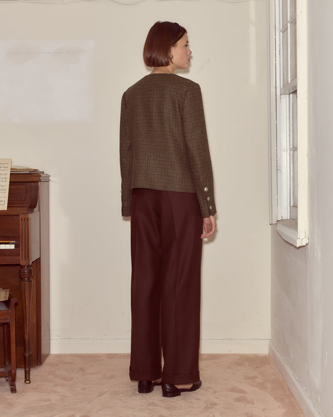 A woman with short hair stands indoors facing a wall, wearing the Morris Houndstooth Rice Jacket and dark trousers.