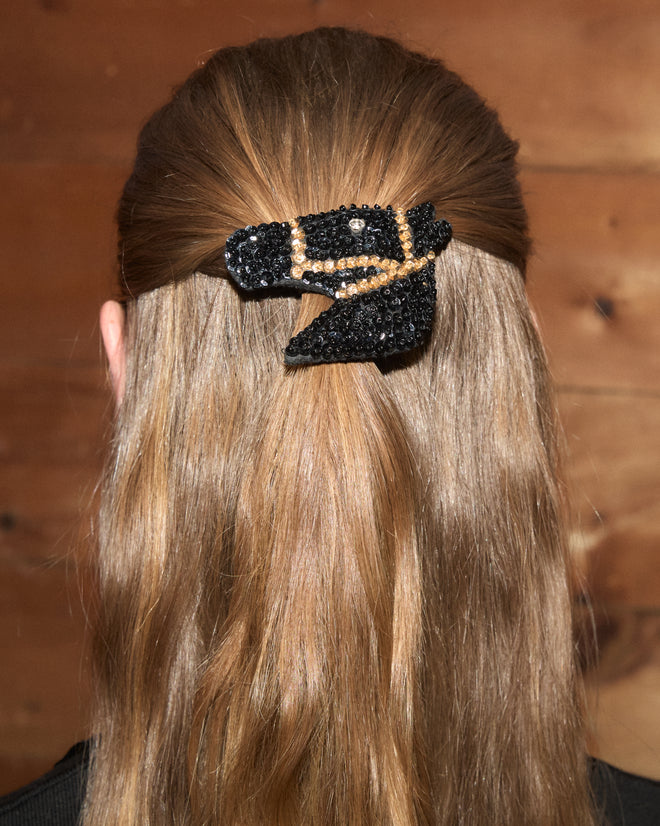 A woman with long hair wears the Sequin Pony Barrette - Black against a wooden background.