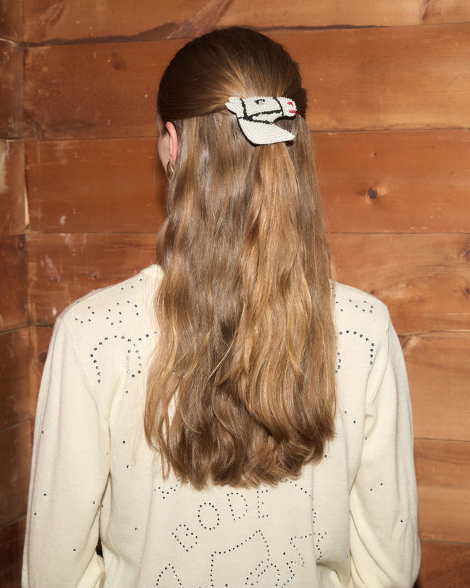 A woman with long wavy hair facing away, wearing a sweater and the Sequin Pony Barrette - Cream clipped in her hair, set against a wooden wall background.