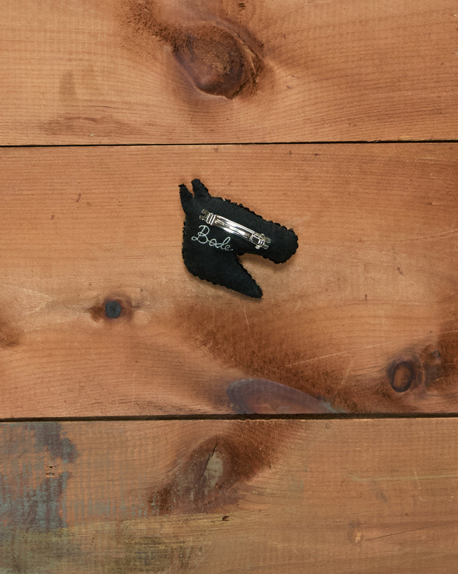 A black Sequin Pony Barrette featuring a sparkling gemstone accent and “Babe” text, displayed on a wooden surface.