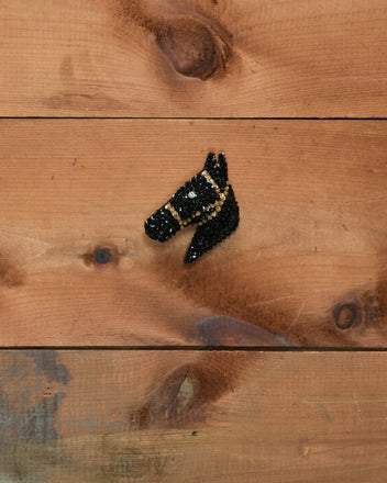 The Sequin Pony Barrette - Black, adorned with shimmering black beads and a sparkling gemstone eye, is displayed on a rustic wooden background.