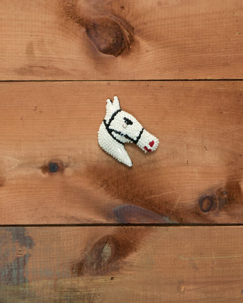Sequin Pony Barrette in cream, adorned with beads and a gemstone eye, displayed on a wooden surface with visible grain and knots.