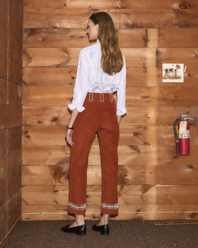 Cheval Corduroy Trousers in rust-colored corduroy with beaded belt loops and embroidered circular hem patterns.