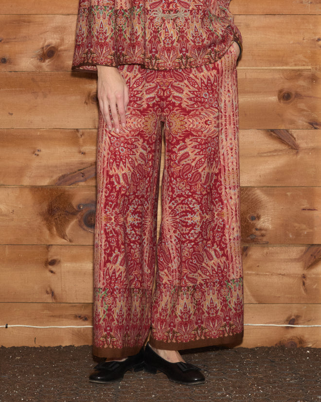 A person wearing Arrowleaf Pants stands in front of a wooden wall.