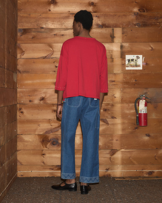 Person wearing the Stables Long Sleeve Tee and blue jeans stands facing a wooden wall with a fire extinguisher and a small photo.