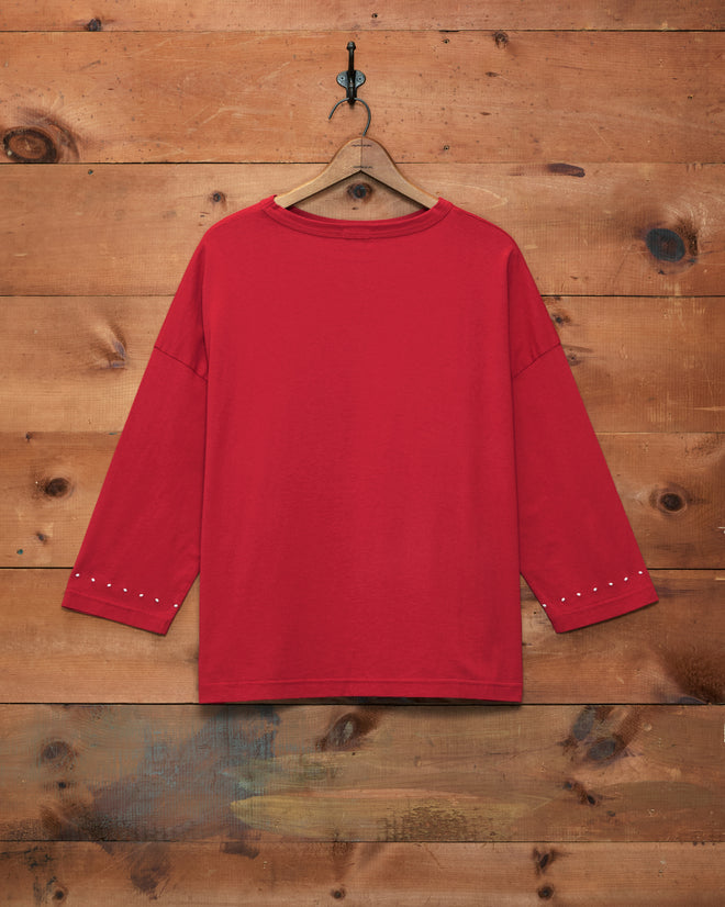 A Stables Long Sleeve Tee, made from 100% cotton in solid red, hangs on a wooden hanger against a wood panel wall.