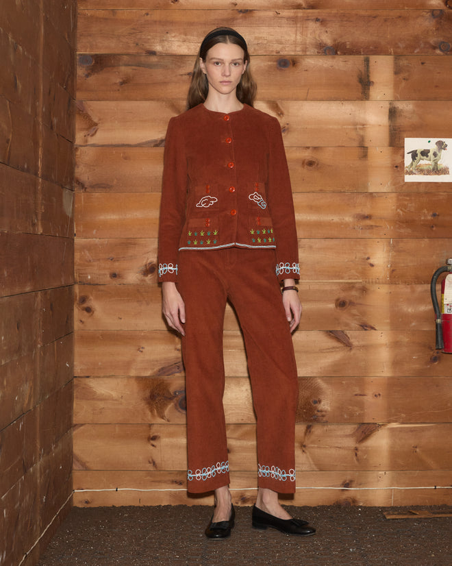 Model wearing a hand-beaded rust-colored Cheval Corduroy Jacket and matching trousers with white embroidered details.