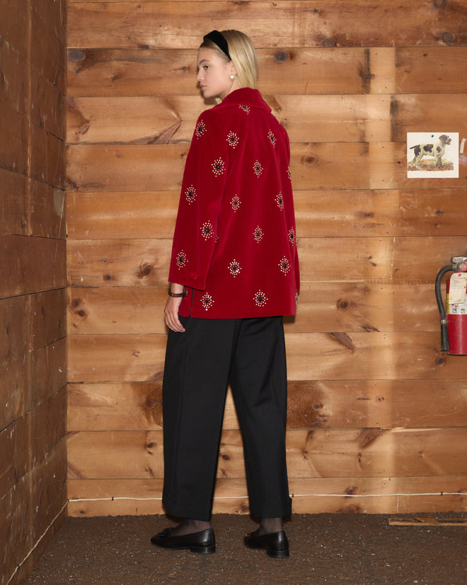Luminaire Jacket in red velvet with floral pearl seed bead detailing, worn with black trousers and loafers.