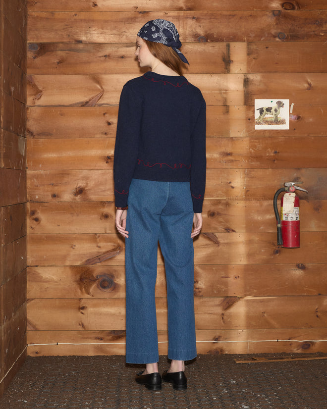 Person wearing a Cowboy Appliqué Pullover, jeans, and headscarf, standing in a wooden room with a fire extinguisher.