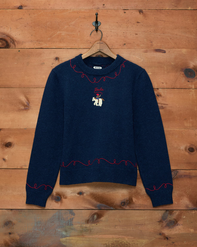 Cowboy Appliqué Pullover in navy blue, featuring red trim, an embroidered dog and “Smile” text, displayed on a wooden wall.
