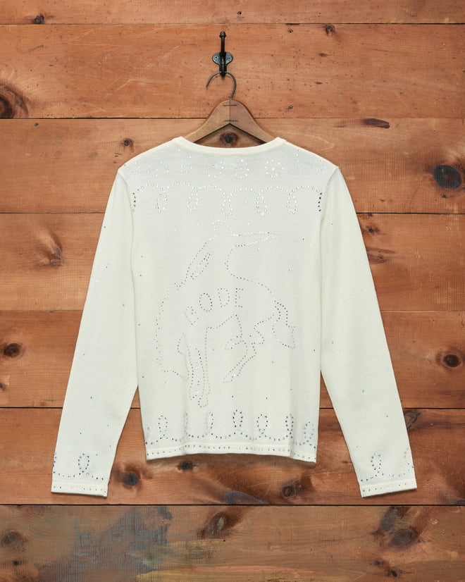 Rodeo Rhinestone Cardigan in cream merino wool, featuring “RODEO” and a cowboy design in rhinestones, displayed on a hanger against a wooden wall background.