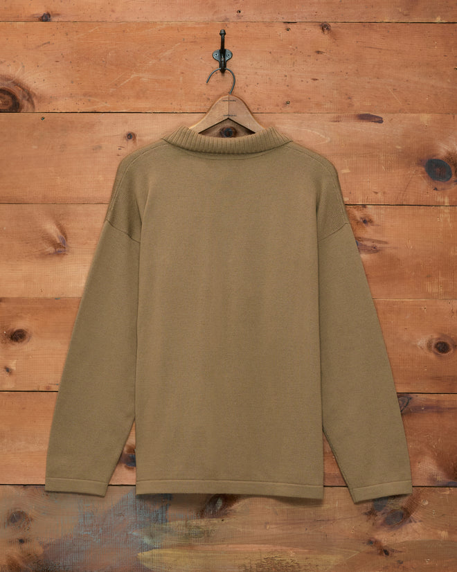 The Cowboy Appliqué Polo - Tan hangs on a hanger against a wooden wall background.