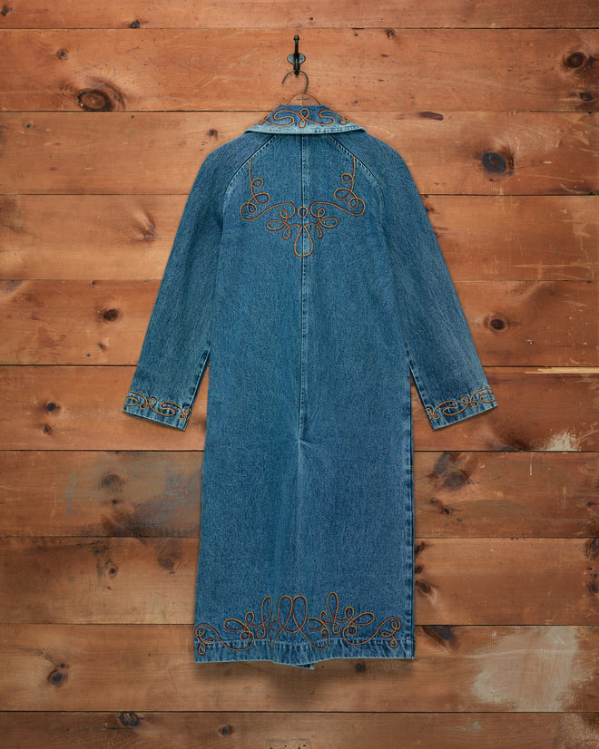 Rawlins Coat—a long-sleeved denim jacket featuring decorative embroidery, displayed on a hook against a wooden wall—makes an ideal choice for young Western jacket enthusiasts.