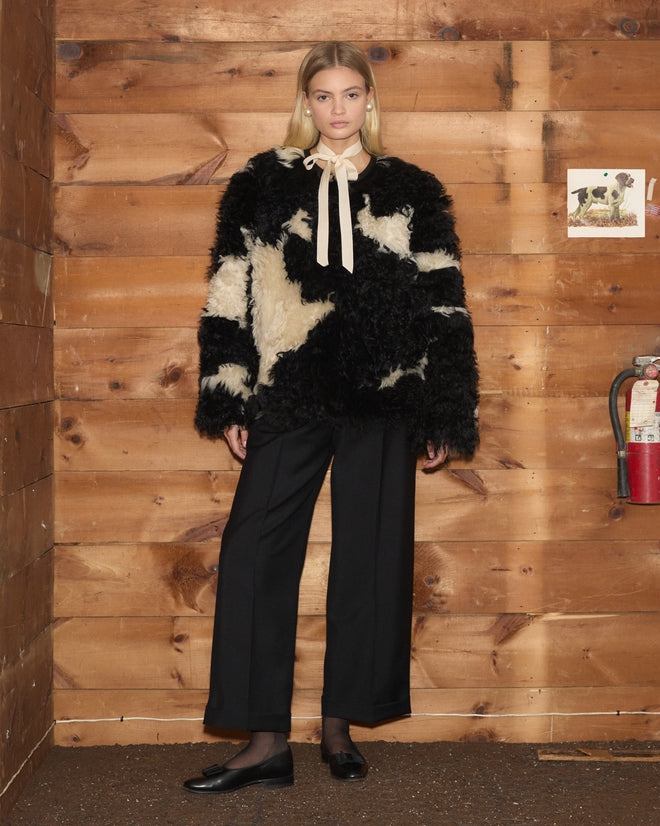 Woman in a Shearling Cow Print Jacket, black pants, and flats stands in a wooden room with a fire extinguisher.
