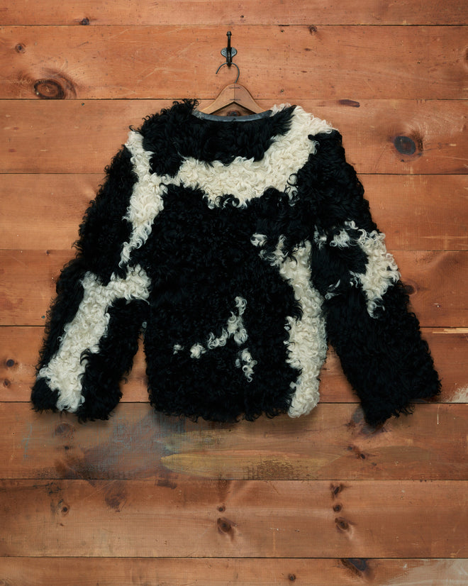 A Shearling Cow Print Jacket in black and white curly faux fur hangs on a wooden wall.