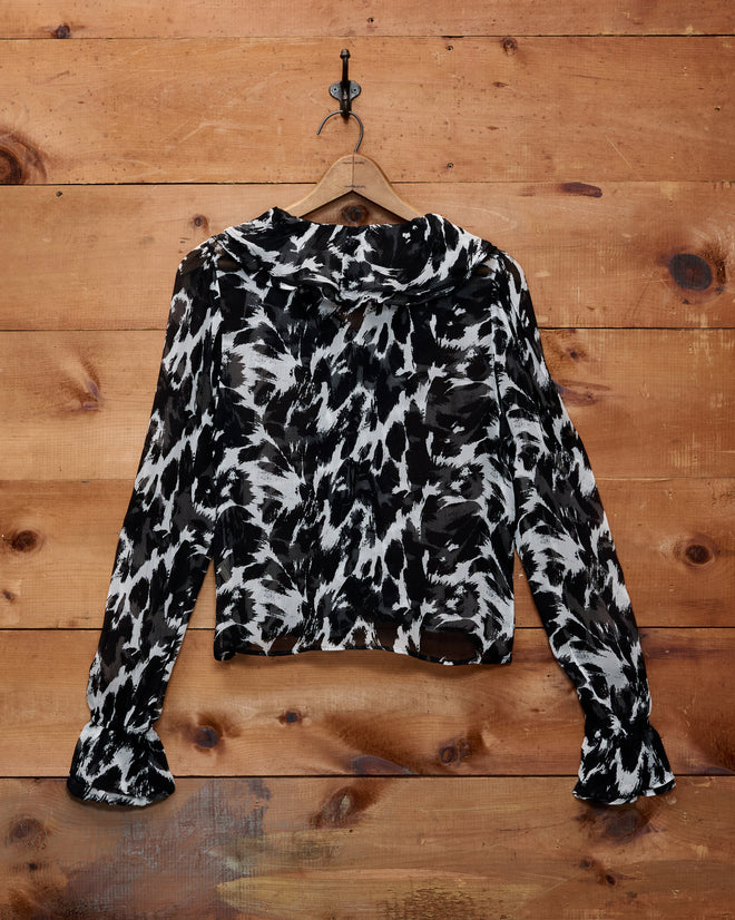 Appaloosa Blouse in black and white silk crepe with spotted pattern, displayed on a wooden wall.