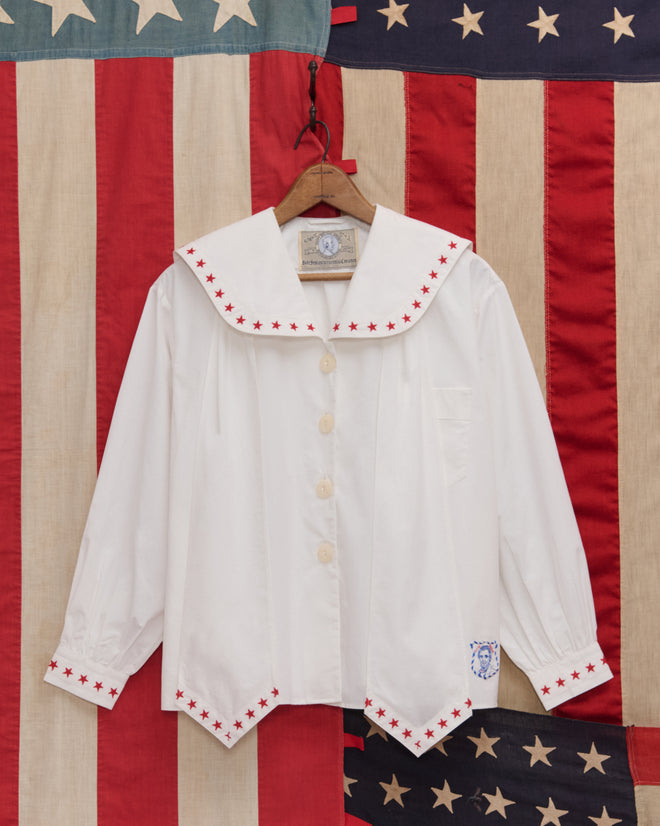 The Red Star Blouse features red star trim on the collar and cuffs, displayed against an American flag—perfect for Liberty costumes or Fourth of July celebrations.