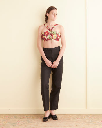 Person standing against a light-colored wall wearing the Kopper Hibiscus Bra, black high-waisted pants, and black shoes.