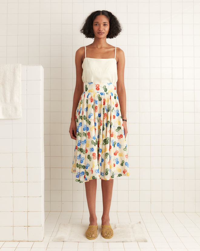 A woman stands on a rug in a tiled room, wearing the Flower Stamp Skirt with floral patterns and textured shoes, inspired by 1920s dress design.