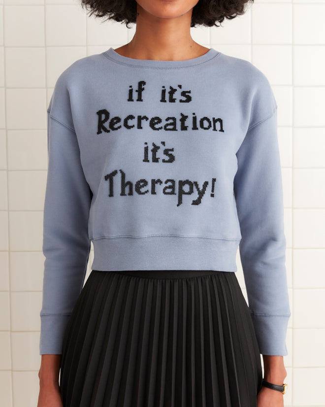 A person models a cropped fit, blue Recreation Crewneck sweatshirt with the slogan 