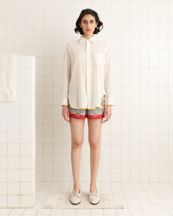 A person in a cream Voile Murray Shirt and patterned shorts stands in a tiled room, facing forward.