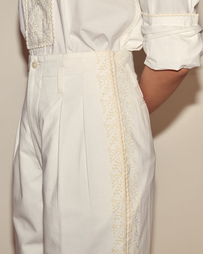 Side view from shoulder to knee of a person wearing wide-leg, high-waisted Closerie Murray Trousers and a white shirt with ivory embroidery.