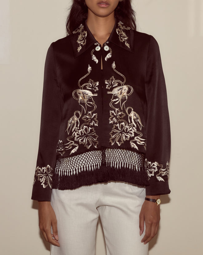 Woman wearing the Phantasm Fringe Jacket in black, styled with white pants and a gold watch, against a plain background.