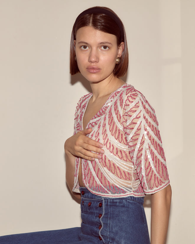 Woman with short brown hair wearing the Beaded Rita Top and high-waisted jeans, seated against a beige wall.