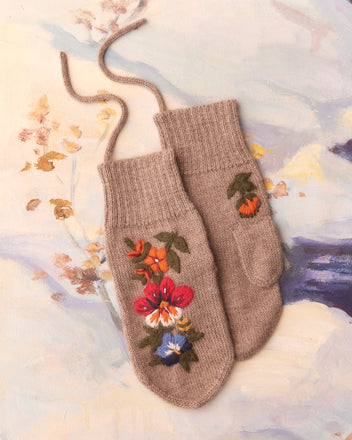 The Wildflower Mittens are crafted from soft baby alpaca and feature a vibrant floral embroidery design set against a textured, artistic background.