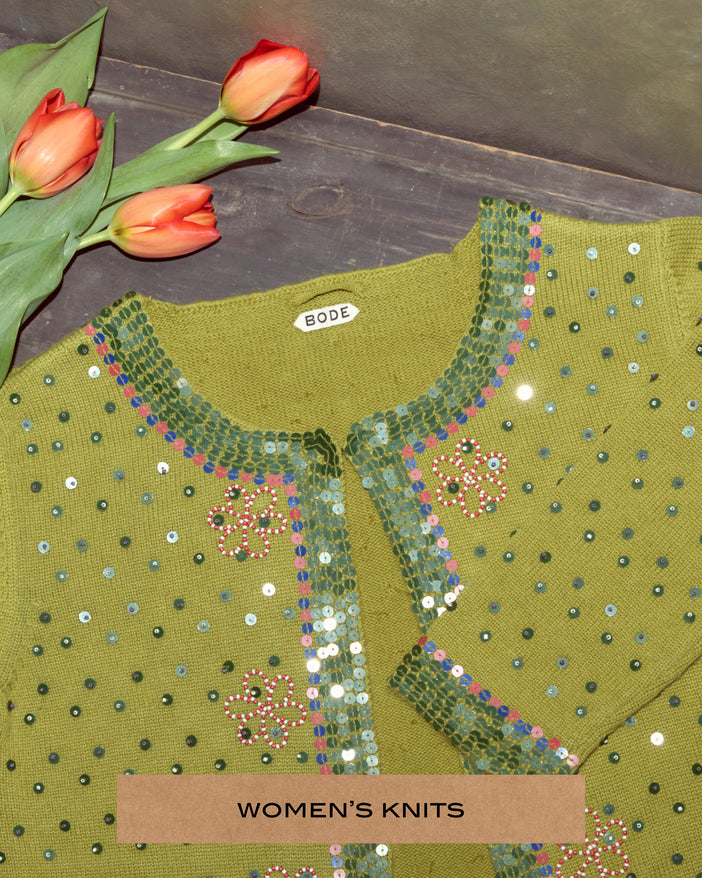 A green cardigan that is embellished with sequins and beads, next to a bouquet of tulips.