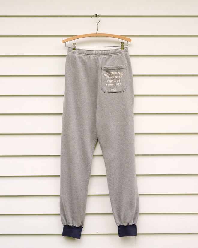 Key Joggers - Grey, crafted from soft loopback terry and featuring a convenient back pocket, hang on a wooden hanger against a white paneled wall—a relaxed essential for rehearsal days at the Yale School of Music or casual strolls to the Norfolk Chamber Music Festival.
