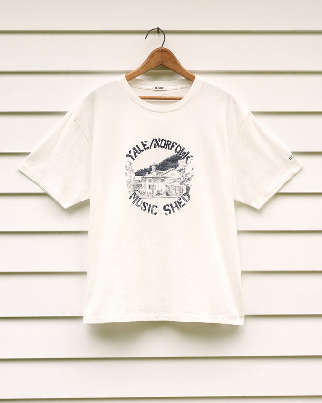 Yale at Norfolk Tee featuring a “Yale Norfolk Music Shed” graphic, displayed on a wooden hanger against crisp white siding—a tribute to the Yale School of Music’s storied legacy and the historic charm honored by the Norfolk Historical Society.
