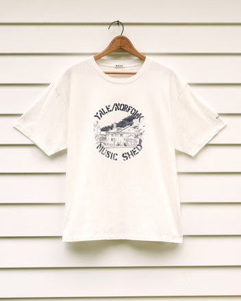 Yale at Norfolk Tee featuring a “Yale Norfolk Music Shed” graphic, displayed on a wooden hanger against crisp white siding—a tribute to the Yale School of Music’s storied legacy and the historic charm honored by the Norfolk Historical Society.