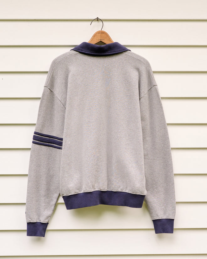 The Yale at Norfolk Polo—a gray loopback terry sweatshirt with navy collar and cuffs, displayed on a wooden hanger against white siding—captures the relaxed, cozy spirit of the Norfolk Chamber Music Festival presented by the Yale School of Music.