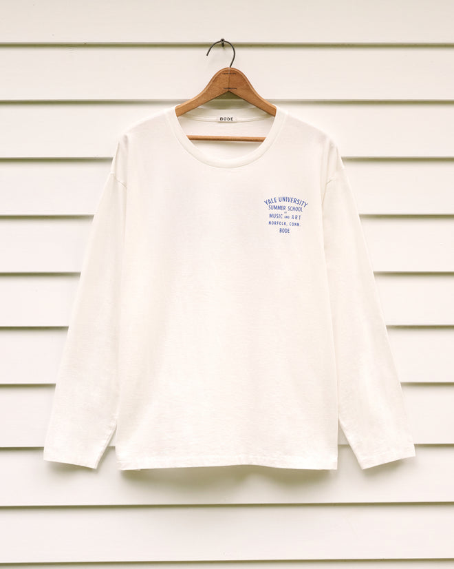 School of Music Tee, a white long-sleeve shirt featuring blue text referencing the Yale School of Music summer program on the chest, displayed on a hanger against a white panel wall.