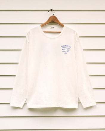 School of Music Tee, a white long-sleeve shirt featuring blue text referencing the Yale School of Music summer program on the chest, displayed on a hanger against a white panel wall.