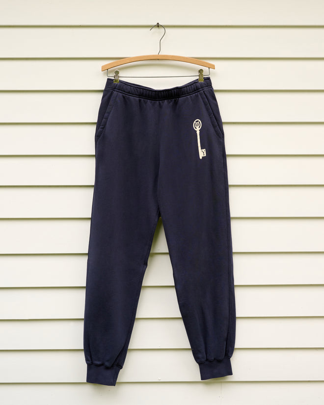 Key Joggers - Blue, featuring a white key design inspired by the Yale School of Music, made from navy blue loopback terry, shown on a wooden hanger against a white wall.