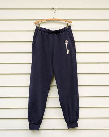 Key Joggers - Blue, featuring a white key design inspired by the Yale School of Music, made from navy blue loopback terry, shown on a wooden hanger against a white wall.