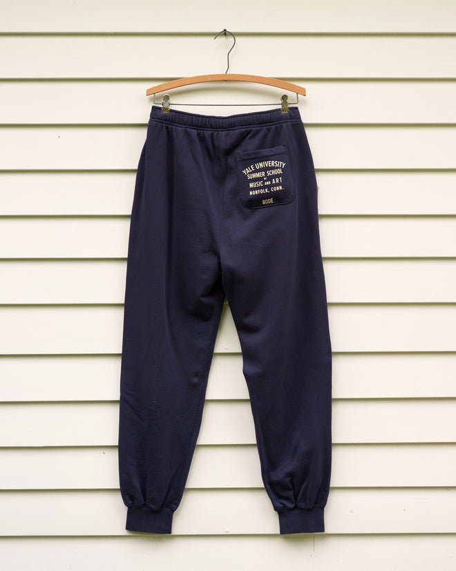 Key Joggers - Blue displayed on a hanger against white horizontal paneling, featuring the Norfolk Chamber Music Festival Yale School of Music logo on the back pocket.
