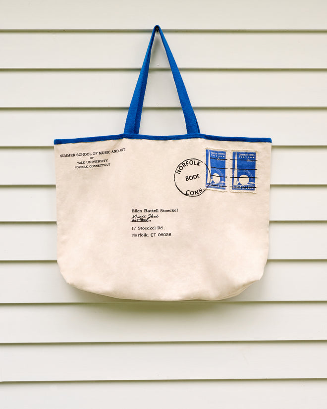 The Yale Postage Tote, designed to resemble a mailed envelope, hangs on a white, horizontally paneled wall—its understated charm conjuring memories of summer sessions at the Yale School of Music’s Ellen Battell Stoeckel estate.