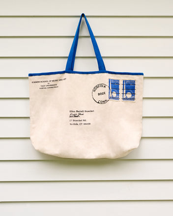 The Yale Postage Tote, designed to resemble a mailed envelope, hangs on a white, horizontally paneled wall—its understated charm conjuring memories of summer sessions at the Yale School of Music’s Ellen Battell Stoeckel estate.