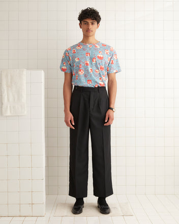 A person wearing the Yearbook Boxy Tee in a vintage-inspired print of blue, paired with black pants, stands against a tiled wall.