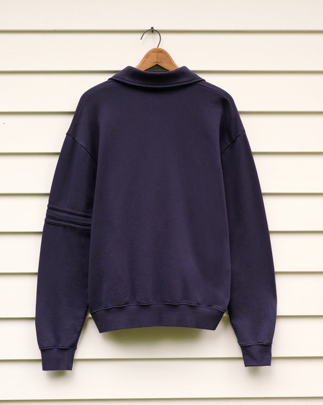 A School of Music Polo on a wooden hanger, displayed against a white paneled wall—ideal for cool evenings at the Norfolk Chamber Music Festival or as a comfortable layer during Yale School of Music’s summer program.