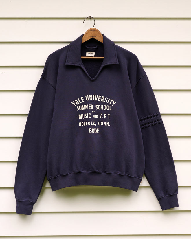 A navy blue School of Music Polo, featuring “Yale University Summer School Music and Art” on the front and inspired by the prestigious Yale School of Music’s summer program, hanging outside.