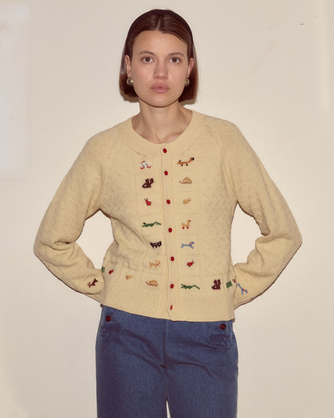 A woman wears the Zoologist Cardigan, a cream knitwear piece featuring small embroidered animal motifs, standing against a plain light background.