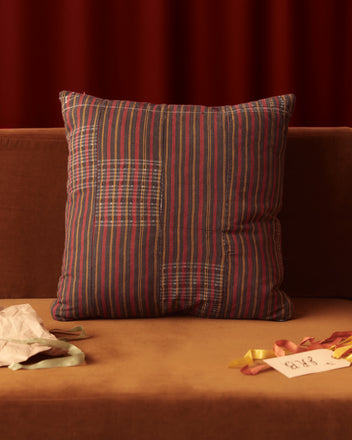 The Firelick Stripe Pillow rests on a brown couch, accompanied by colorful ribbons and a card, showcasing an exquisite touch of home goods charm.