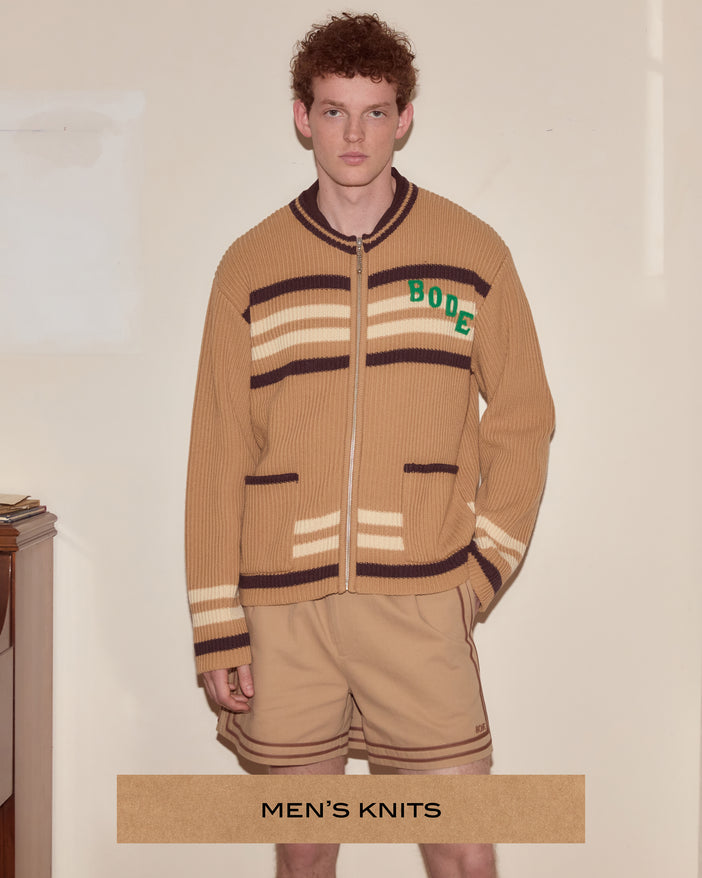 A man wearing a tan/brown zip up cardigan that says "Bode" in green on the chest.