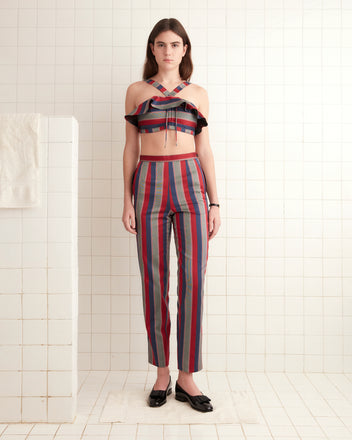 A woman wearing the Marina Stripe Bra and matching pants stands on the tiled floor of a white room.