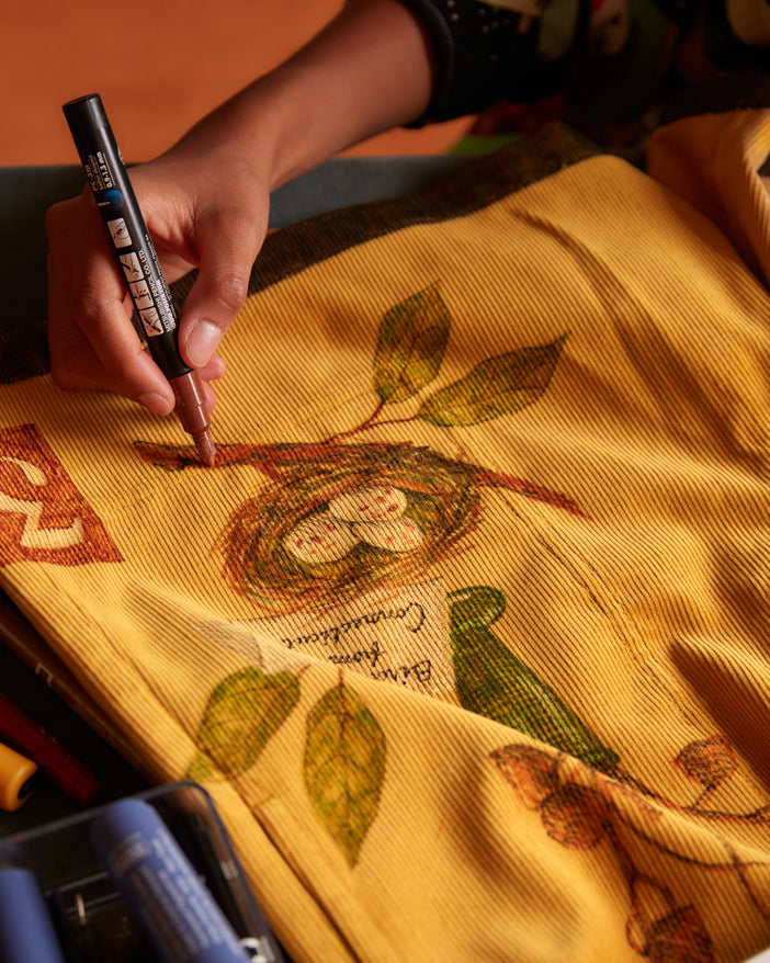 person drawing on corn-colored British corduroy with hand-drawn illustrations in color