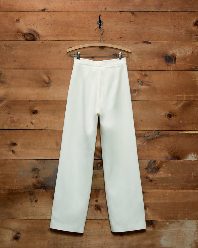 Cream Riding Twill Sailor Trousers in a 1940s wide-leg style hanging on a wooden hanger against a wooden wall.